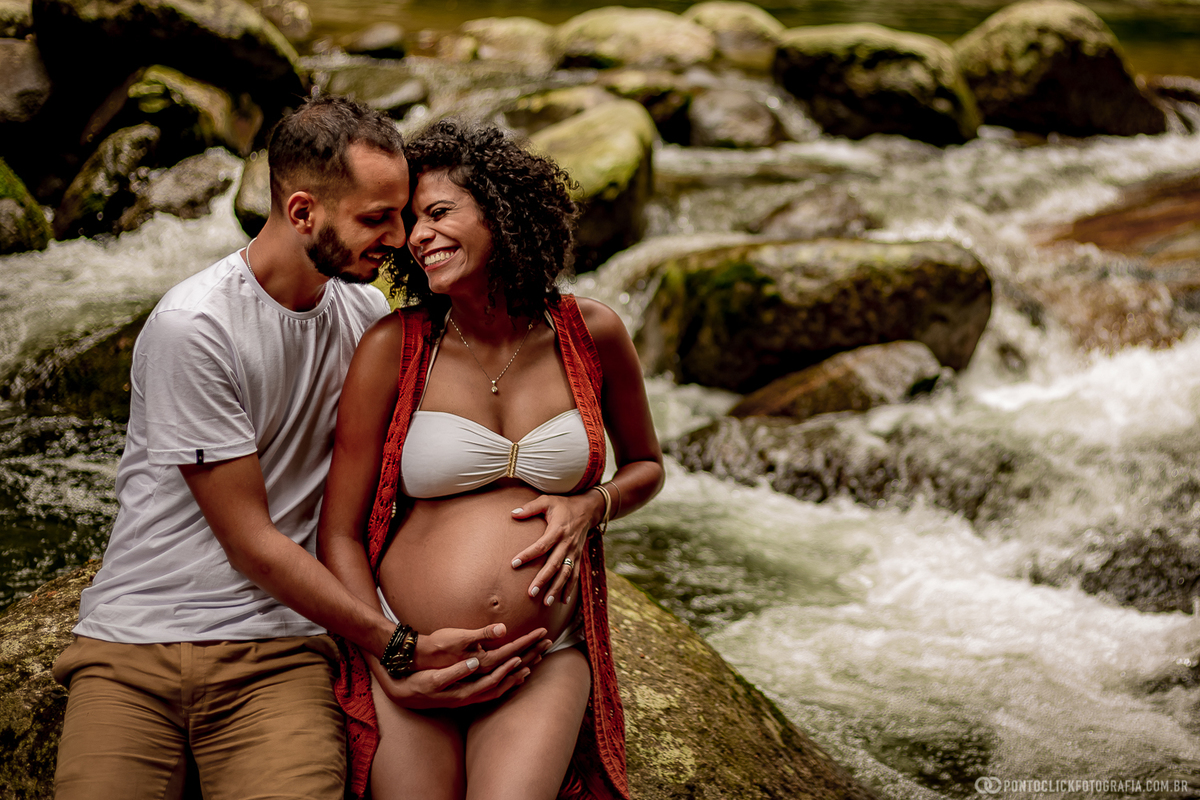 casal sentado na pedra da cachoeira em ilhabela segurando a barriga