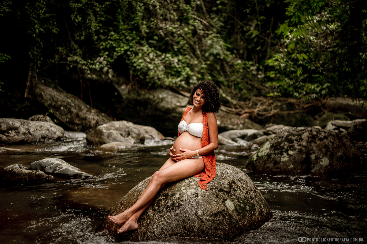 mamae sentada na pedra da cachoeira em ilhabela segurando a barriga