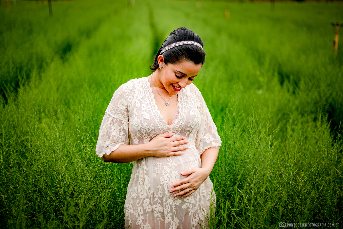 sessão de fotos com gestante em holambra gestante esta com as maos na barriga olhando pra barriga e sorrindo no meio das flores verdes em holambra cidade das flores
