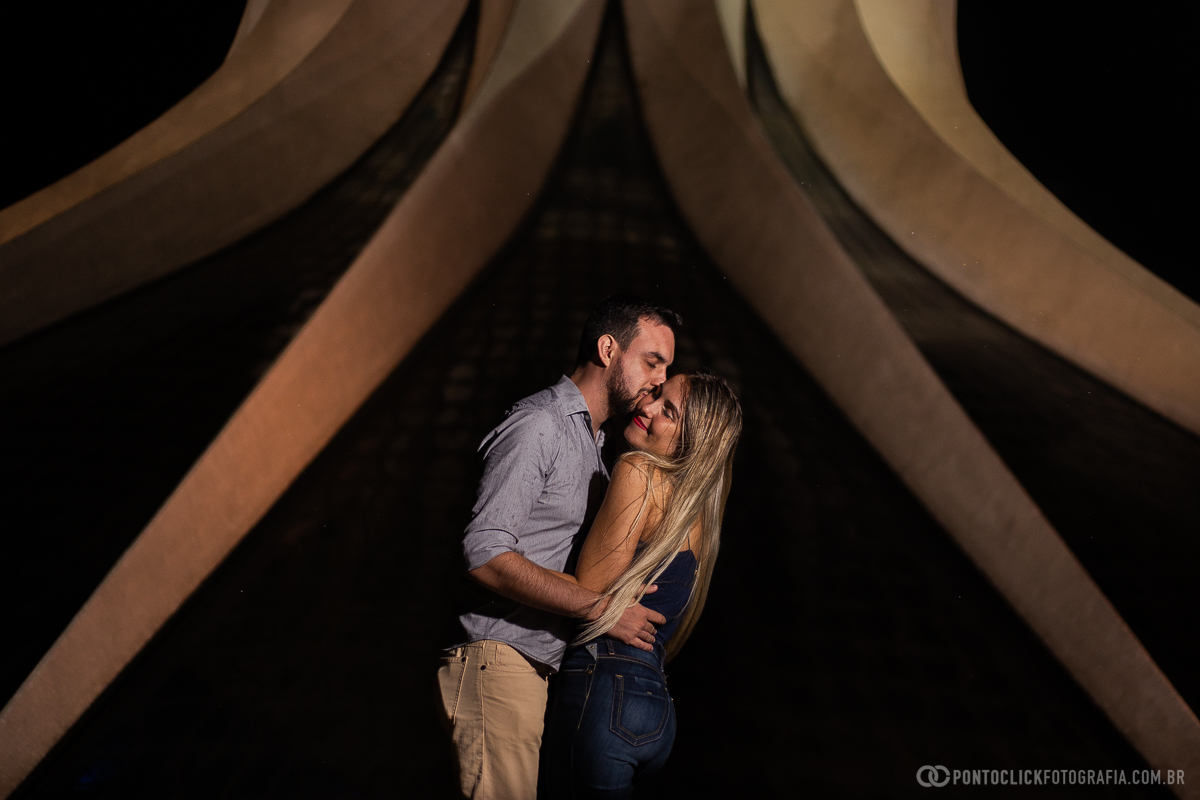 casal abraçado e noivo beijando a noiva em frente a catedral de brasilia em ensaio fotografico 