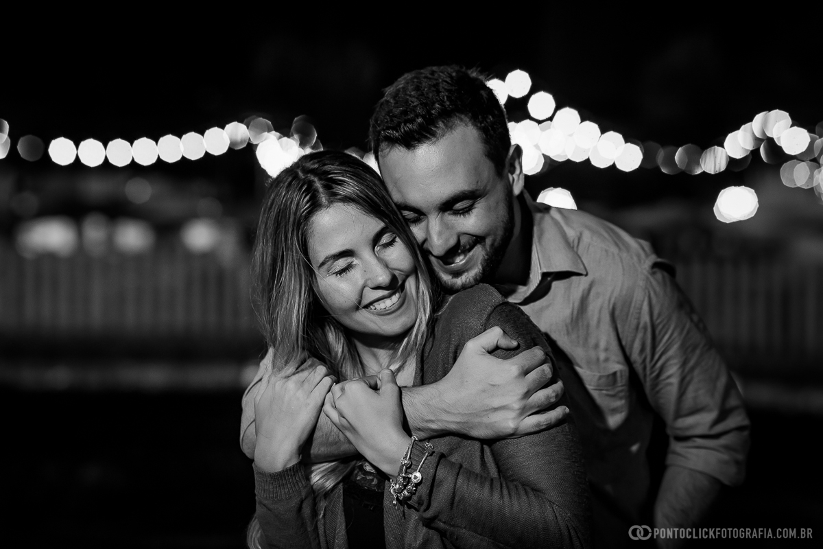 noivo com uma das maos abraçando a noiva por cima e a noiva segurando o braço do noivo e sorrindo em ensaio fotografico noturno em brasilia