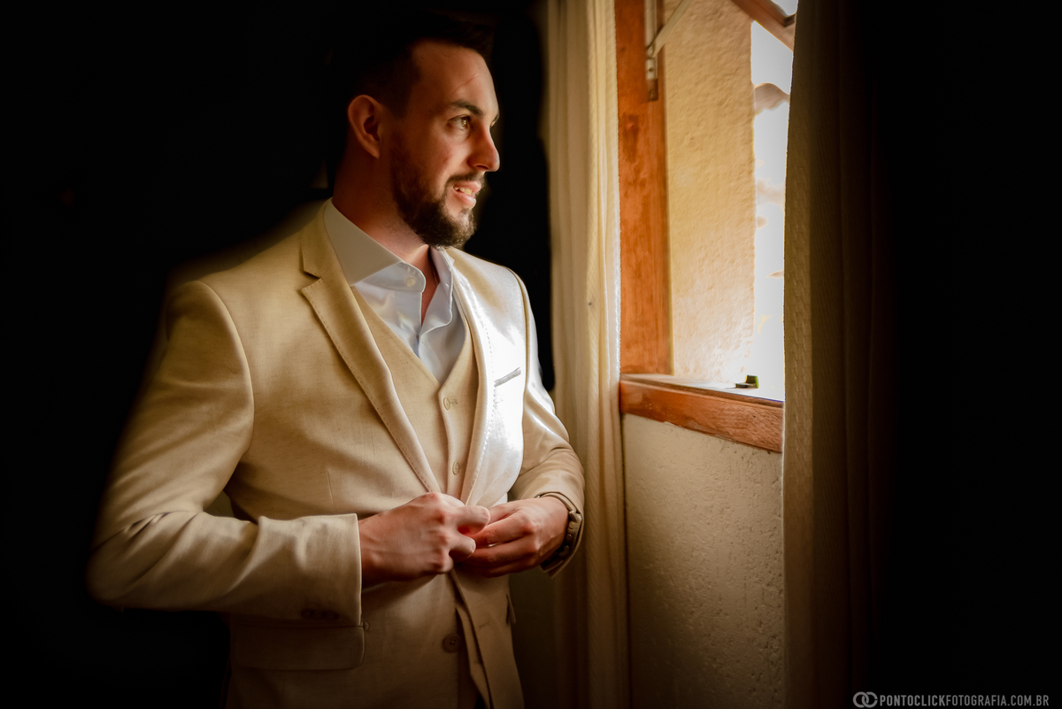 noivo abotoando o terno de noivo em frente a janela do quarto do noivo do espaço laforet em sao roque são paulo