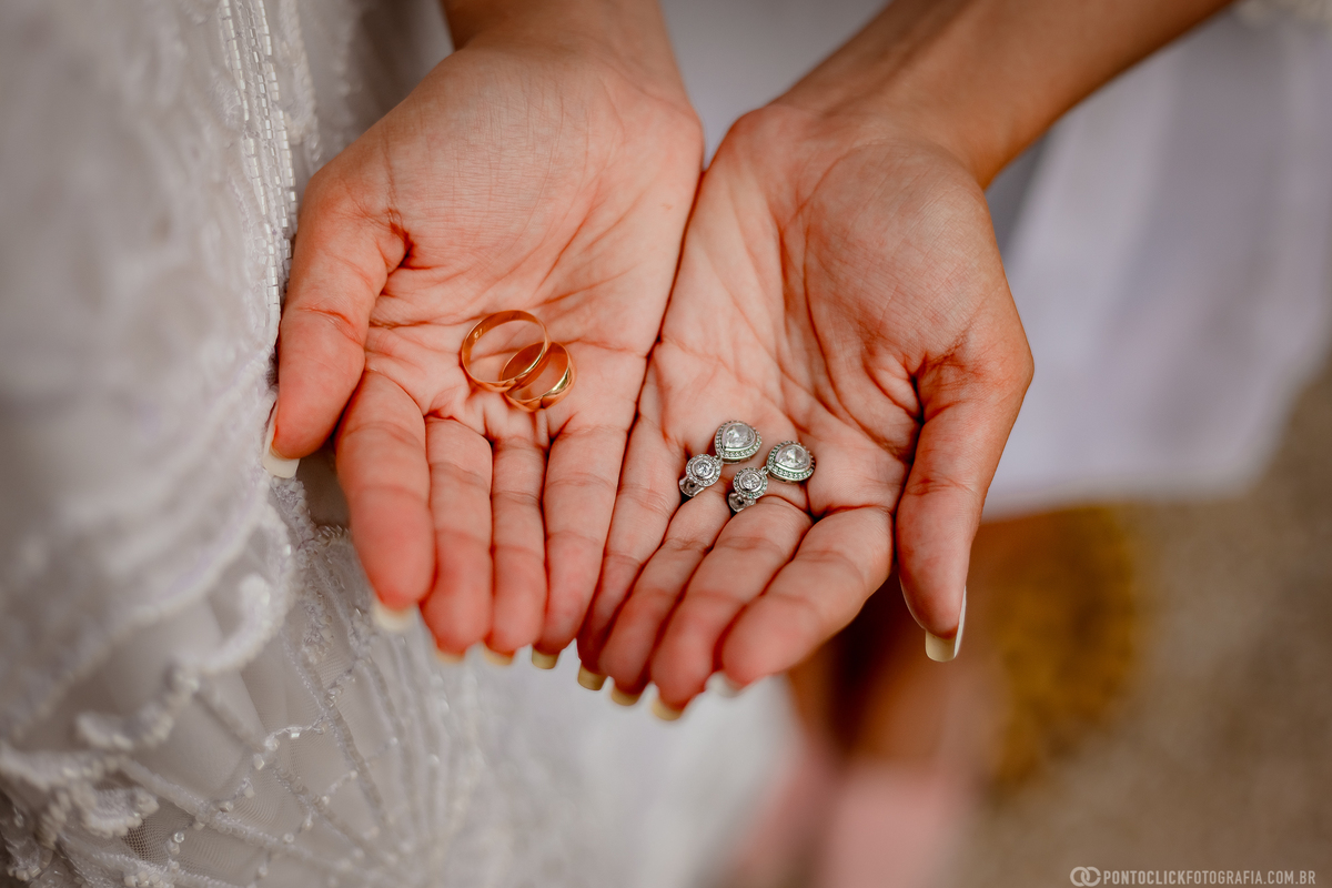 noiva segurando as alianças de casamento e os brincos com seu vestido do lado esquerdo