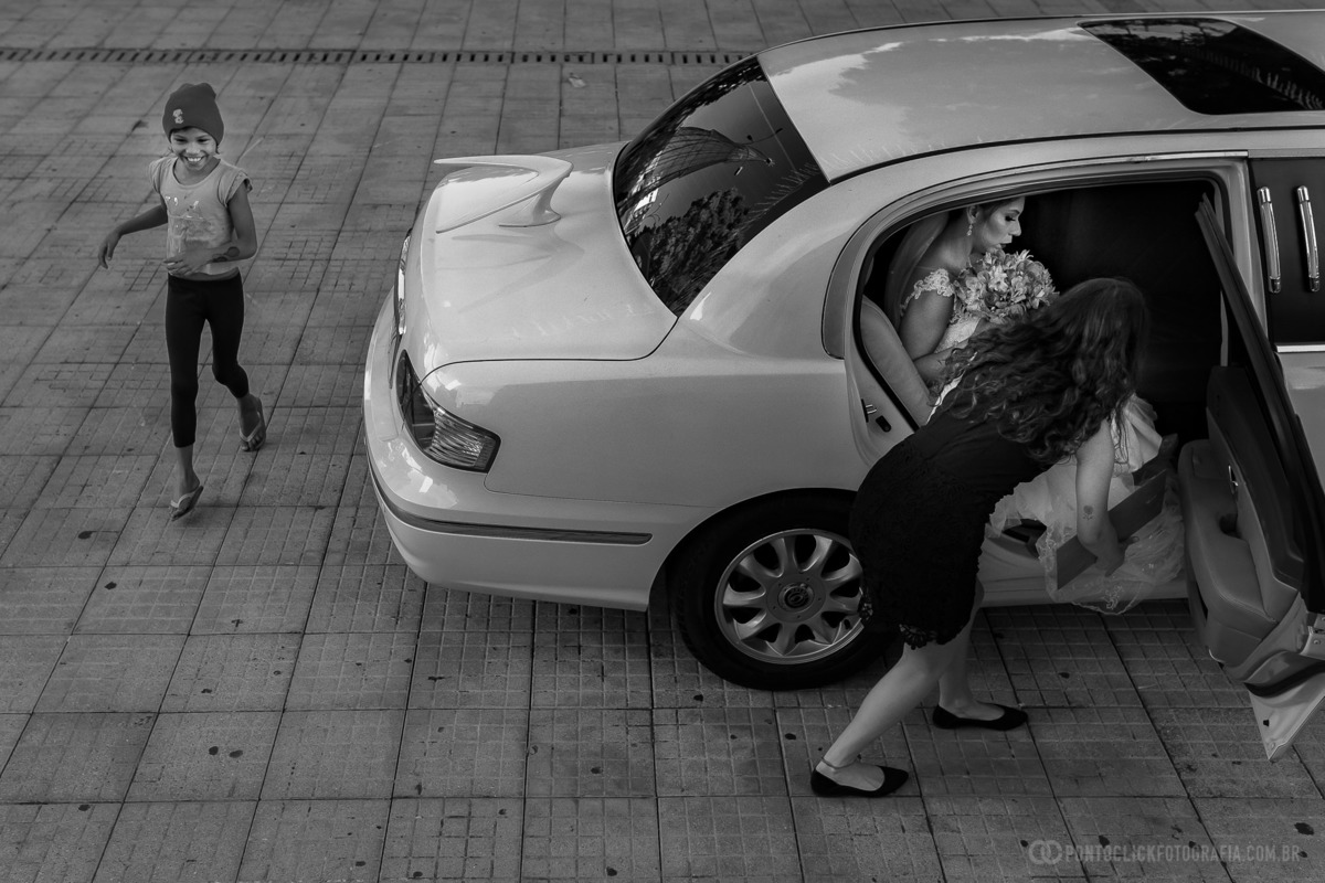 noiva dentro do carro segurando o buque assessoria ajudando para que ela sai do carro e uma criança andan e sorrindo