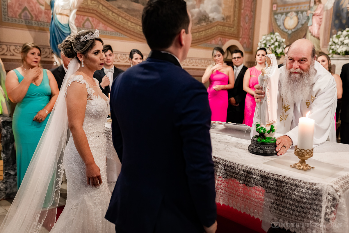 padre segurando a imagem da nossa senhora noiva com vestido brando mae da noiva com vestido azul madrinhas com vestido rosa e vermelho noivo com terno azul escuro 