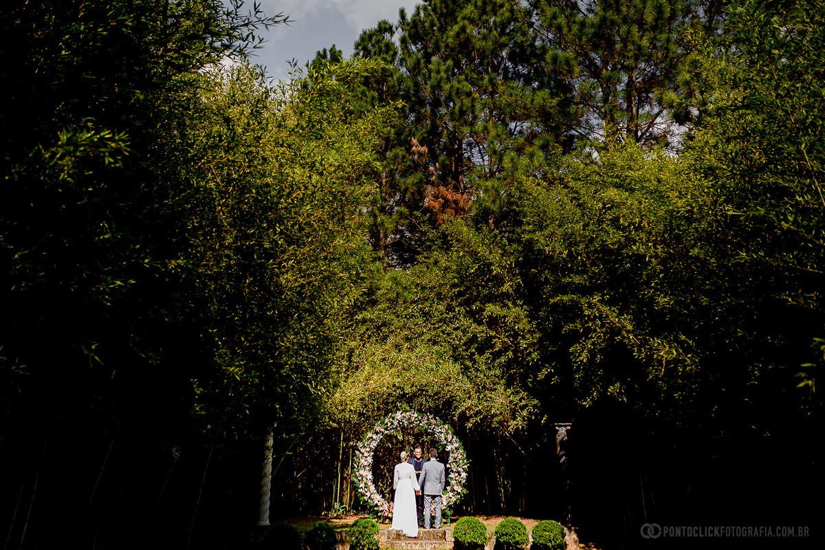casal olhando para o celebrante Jovem Celebrante no e um arco lindo de flores no Elopement Wedding
