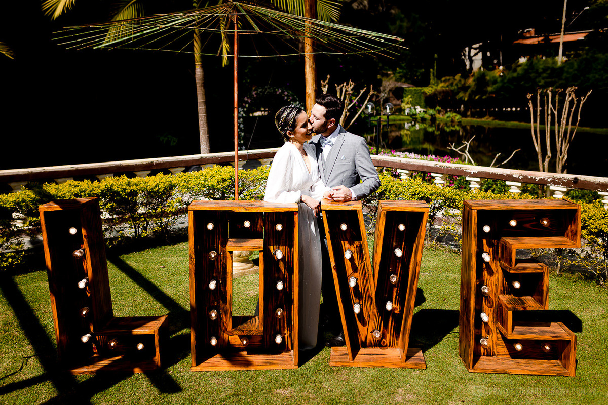 noivos se beijando e embaio um letreiro com a palavra LOVE no Elopement Wedding no Espaço Laforet