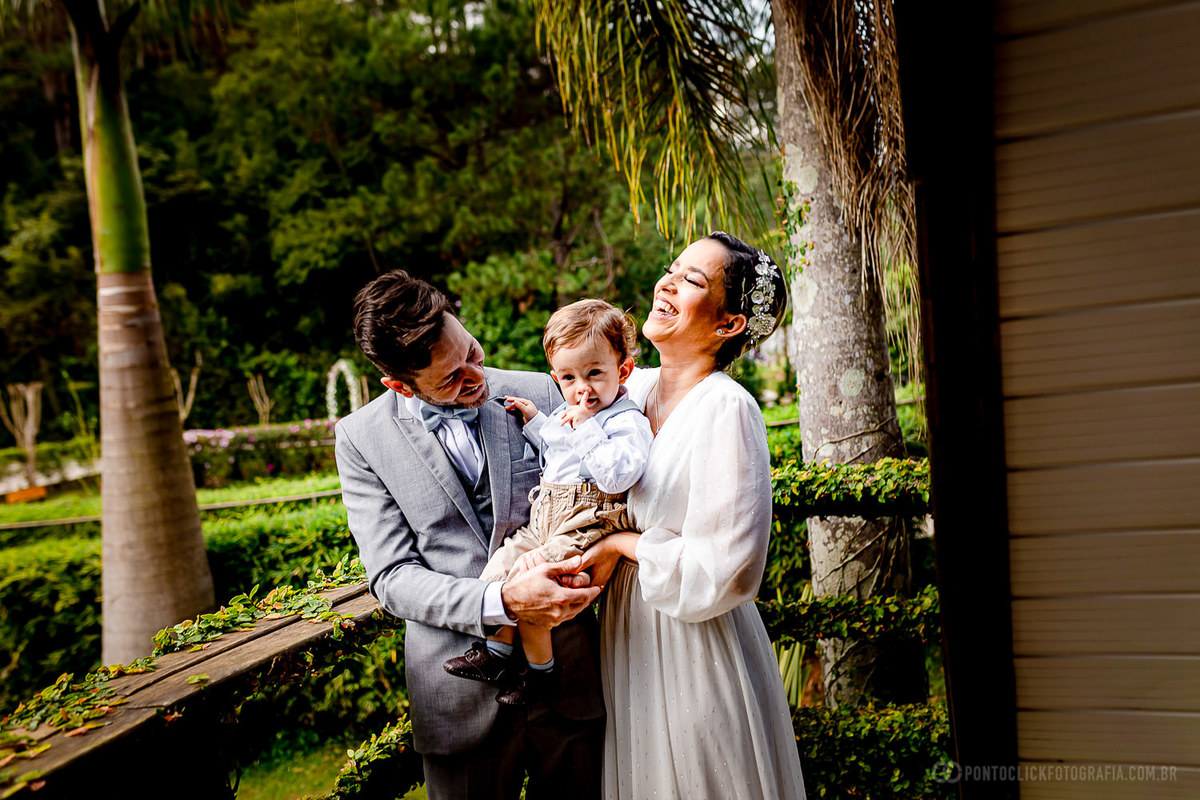 noivos segurando bebe pajem que esta com o dedo no nariz noivos estao sorrindo muito noivo