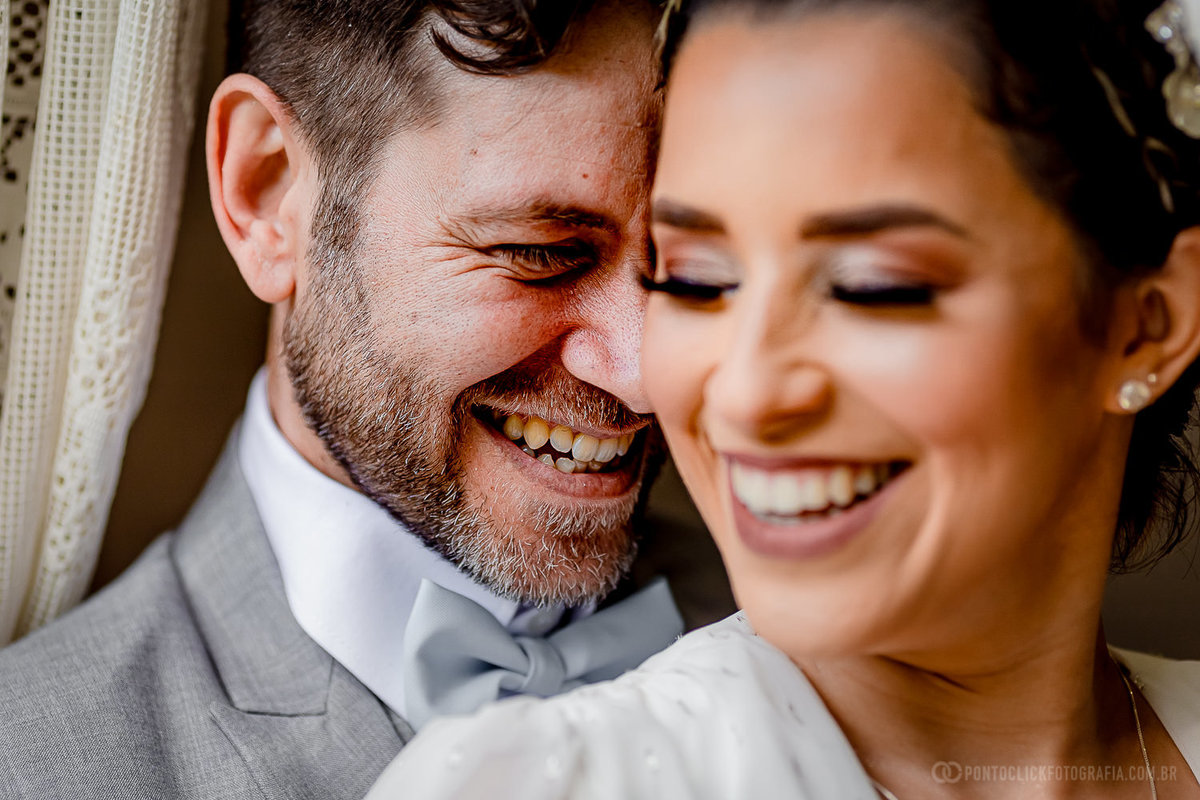 noivos sorrindo e noivo em foco abraçando a noiva