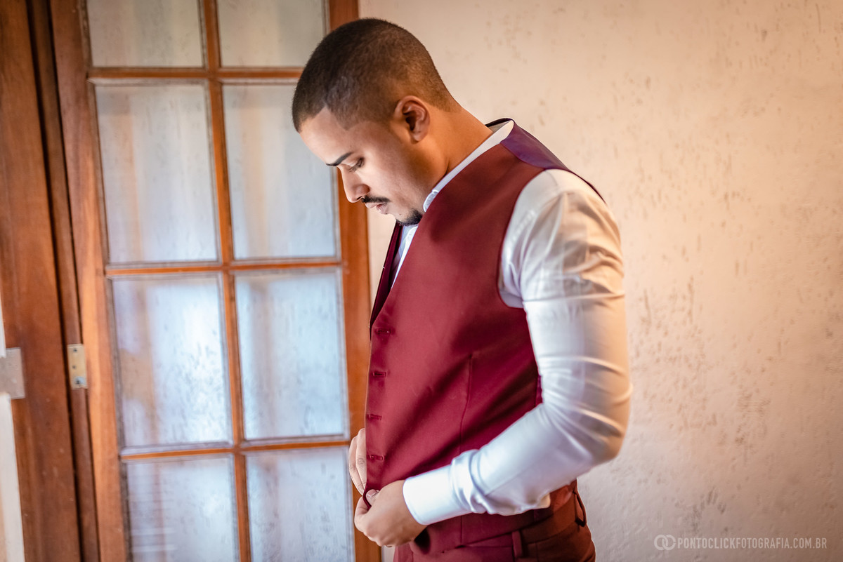 noivo abotoando o colete olhando para fora da janela no quarto do noivo no espaco laforet