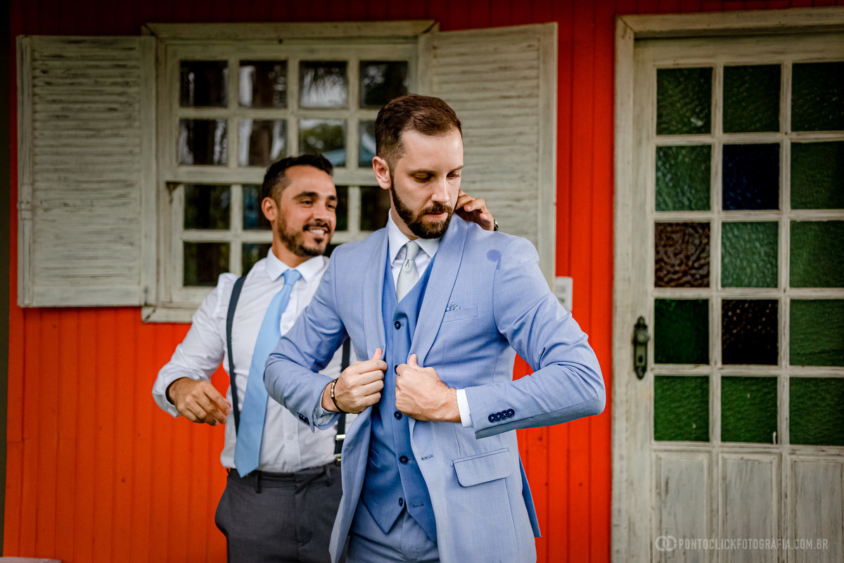 noivo com as maos fechando o terno e padrinho ajudando