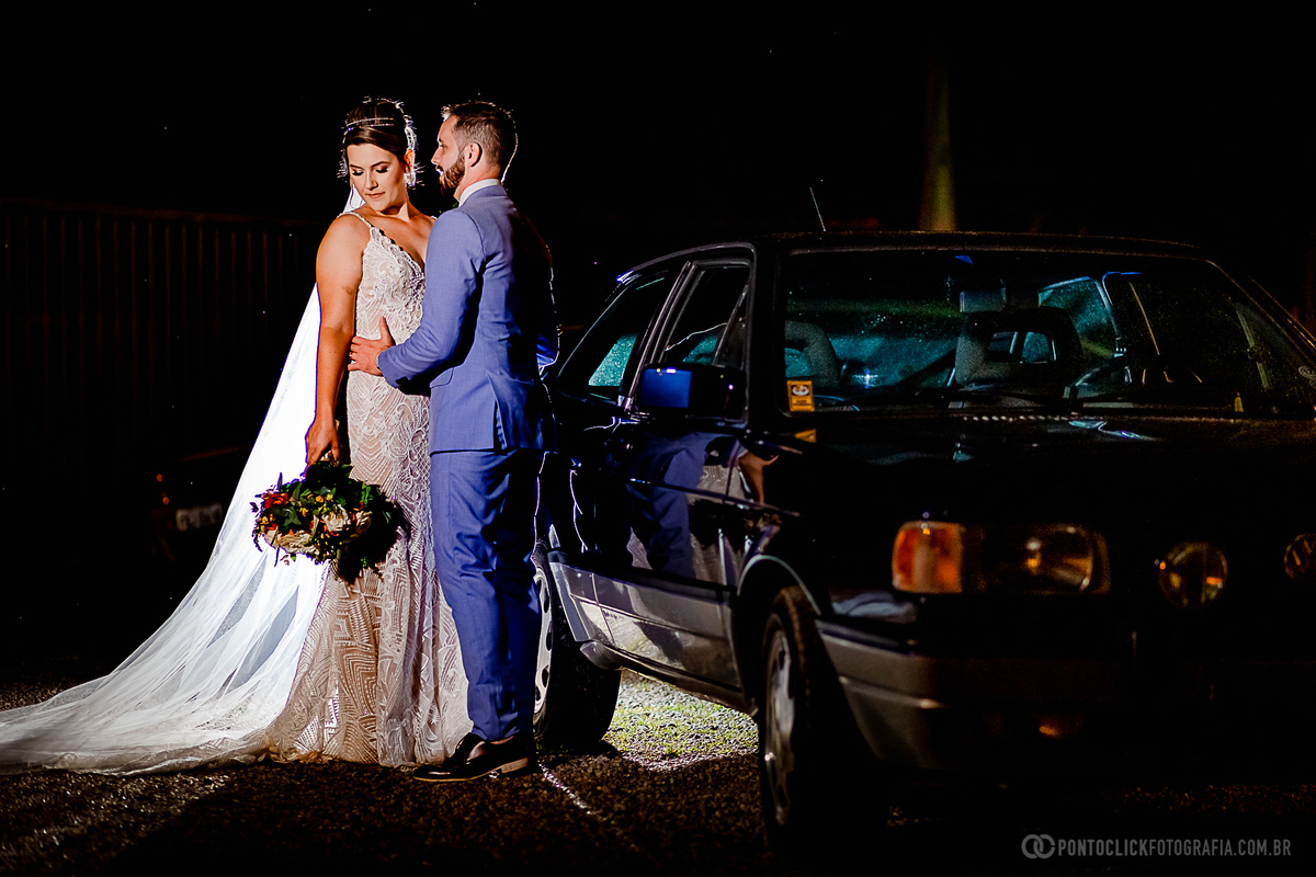 noivo de frente pra noiva segurando na cintura da noiva segurando o buque