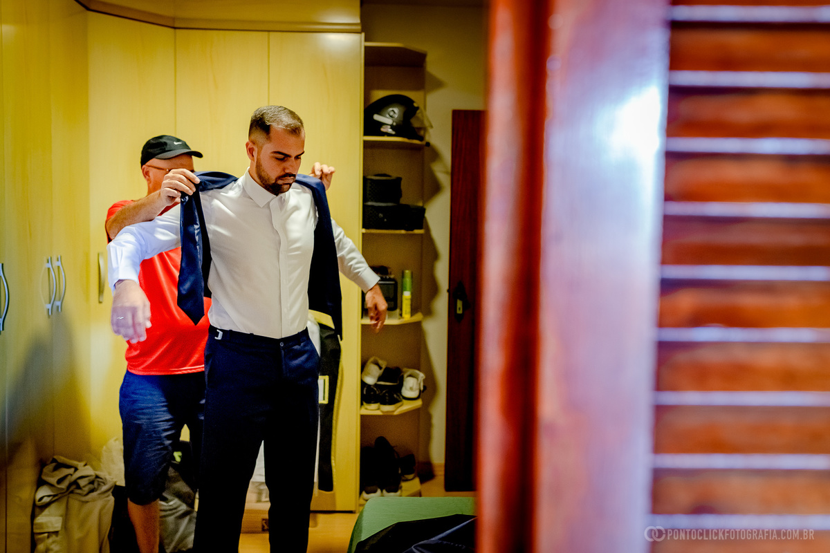 pai do noivo colocando o colete do terno no noivo