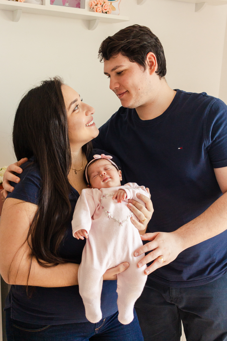 Foto dos pais com filha no colo dando beijo e carinho no ensaio em casa realizado na zona leste da cidade de São Paulo
