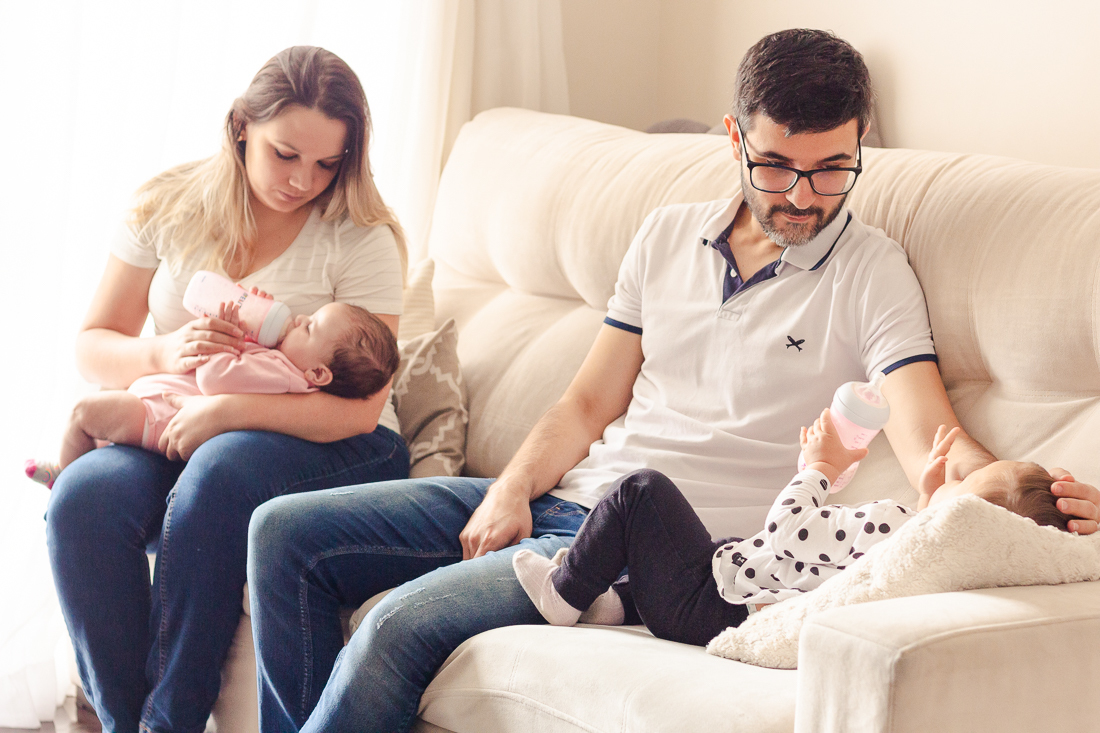 Foto dos pais com filhas no colo dando mamadeira no ensaio lifestyle de família realizado na cidade de São Paulo