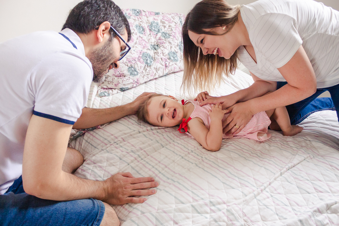 Foto de pais de menina brincando no quarto dos pais em casa, no ensaio de família lifestyle em São Paulo