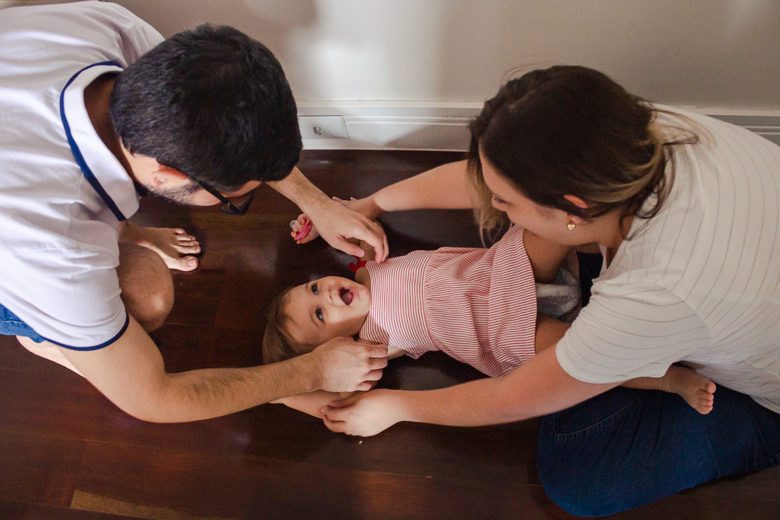 Foto de pais de menina brincando na sala de casa, no ensaio de família lifestyle em São Paulo