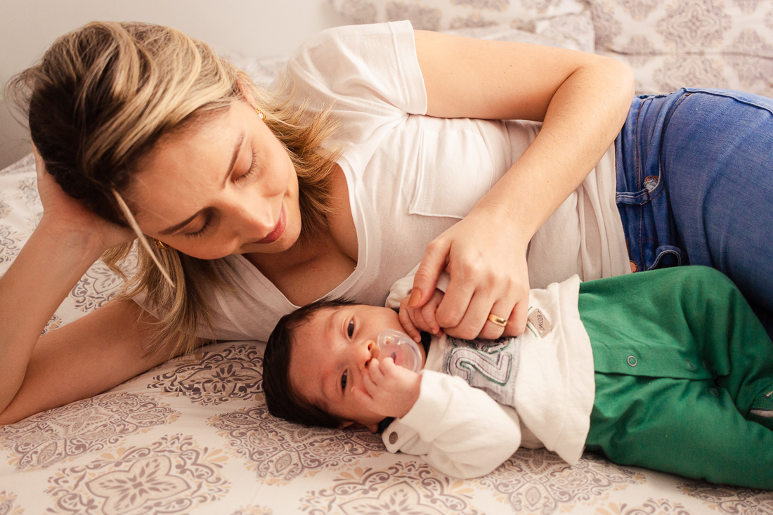 Mãe e filho deitados com a mãe segurando a mão do bebe