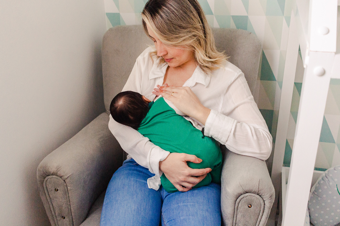Mamãe de primeira viagem sentada amamentando o filho bebe no quarto, no ensaio de família em casa, na cidade de São Paulo
