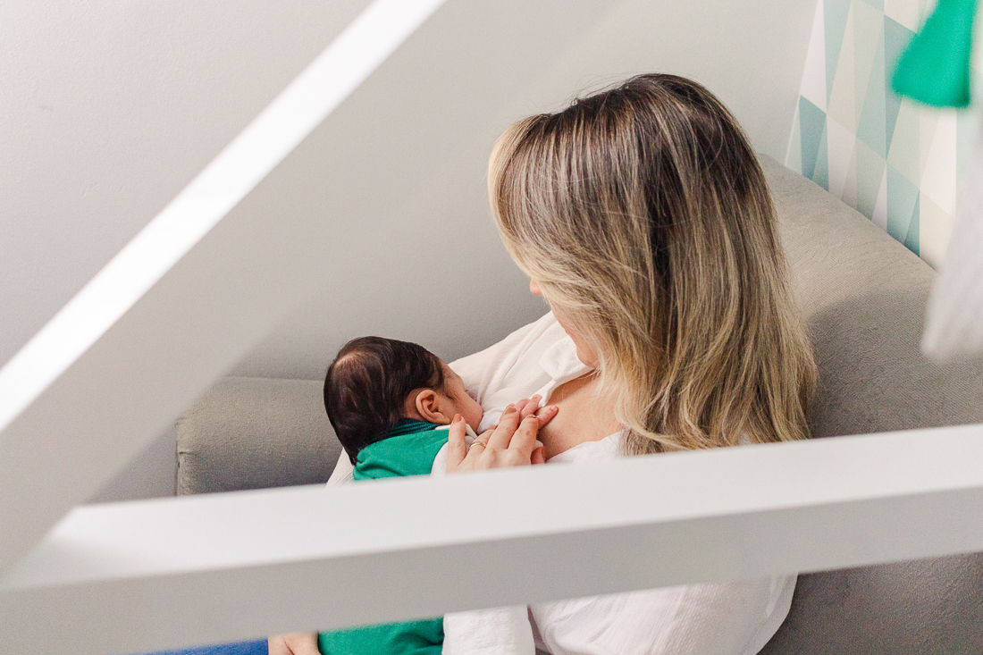 Mamãe de primeira viagem amamentando o filho bebe no quarto, no ensaio de família em casa, na cidade de São Paulo