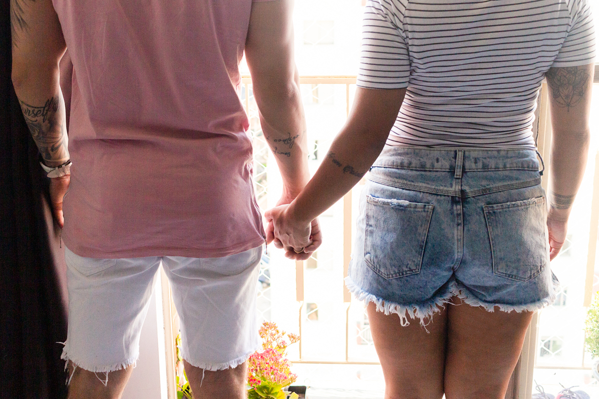 Foto do casal de mãos dadas com vista para a janela do apartamento na cidade de SP