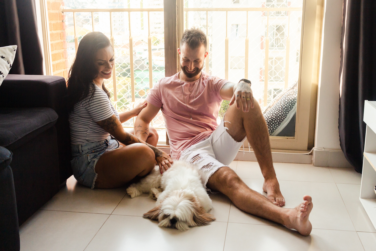 Foto do casal no chão da sala de casa se beijando e fazendo carinho no cachorrinho, no ensaio lifestyle na cidade de SP