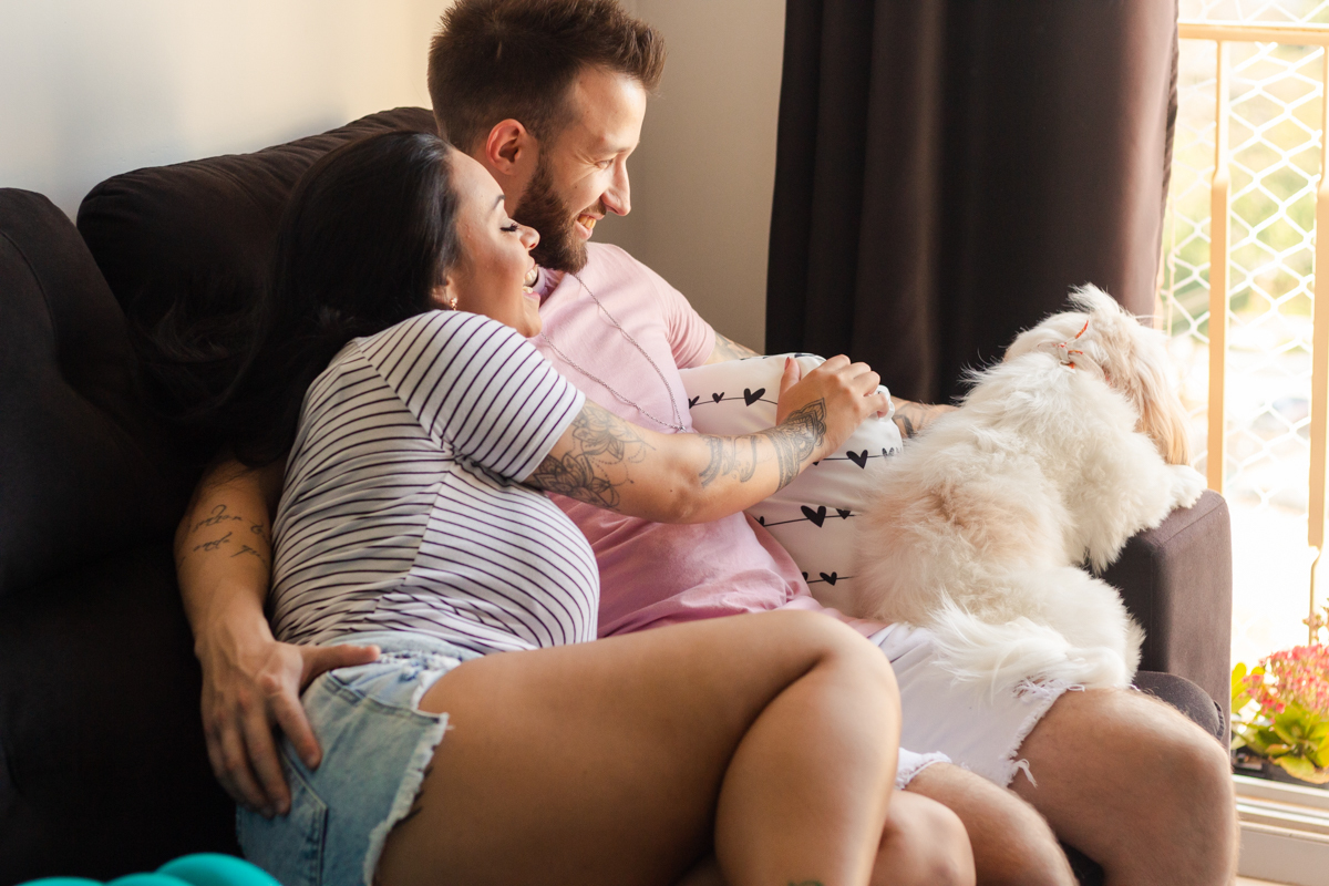 Foto do casal no sofá de casa com o cachorrinho fazendo carinho, no ensaio lifestyle na cidade de SP