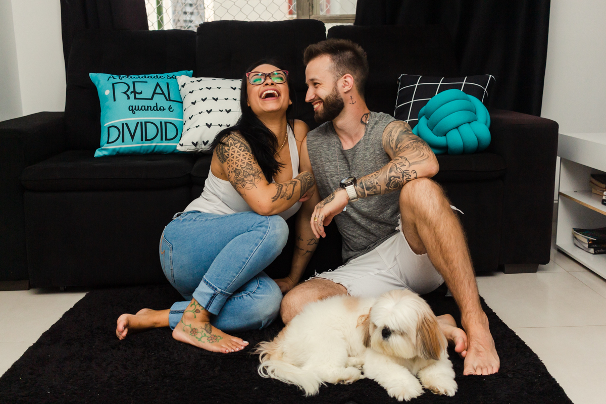 Foto do casal  e cachorro no chão da sala de casa, sorrindo espontâneo no ensaio lifestyle na cidade de SP
