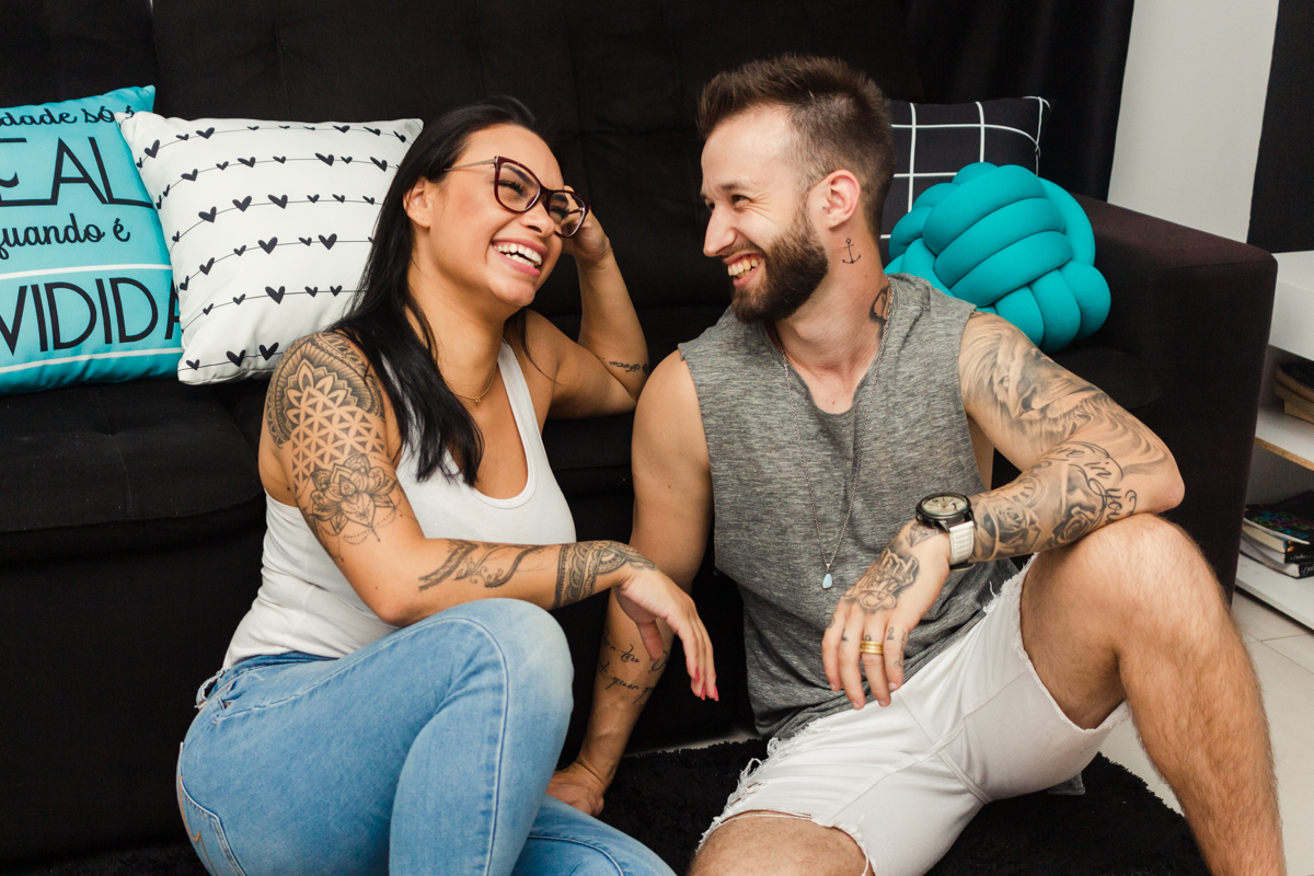 Foto do casal  e cachorro no chão da sala de casa, sorrindo espontâneo no ensaio lifestyle na cidade de SP