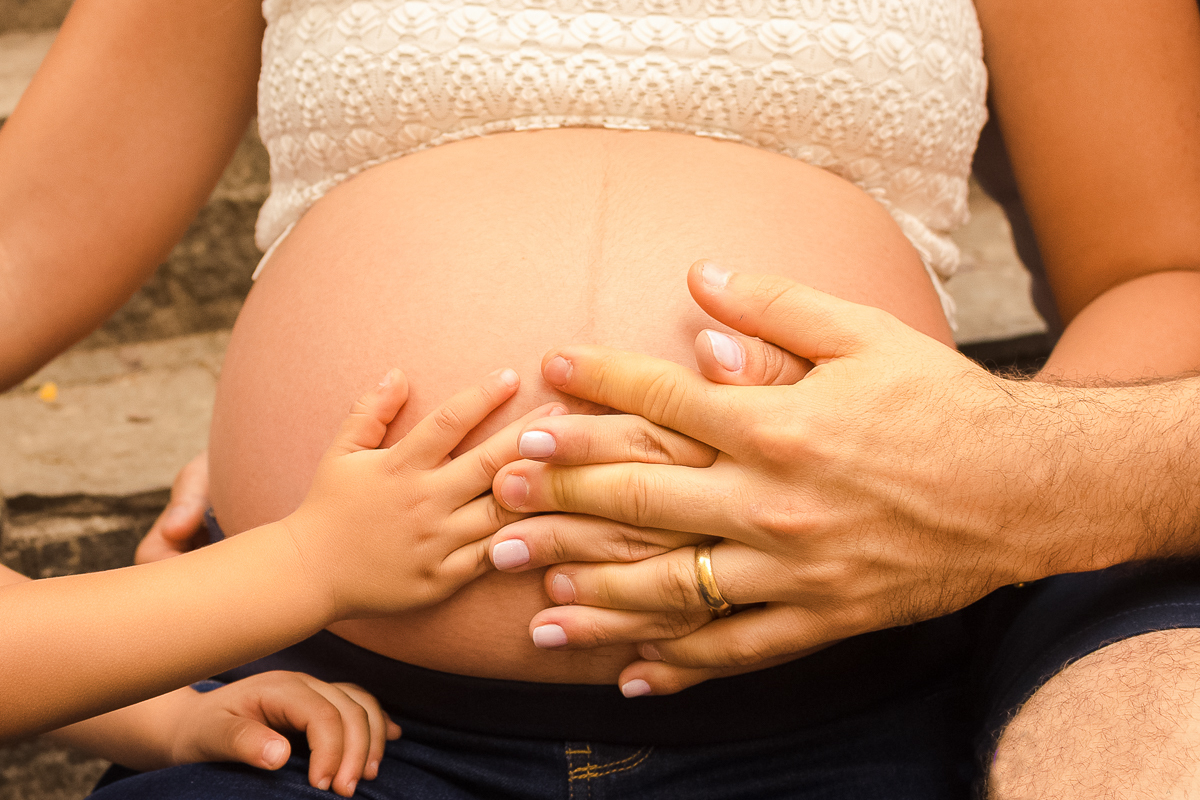 Detalhe barriga de gravida com as mãos dos pais e do filho, no ensaio externo no parque da agua branca na cidade de São Paulo