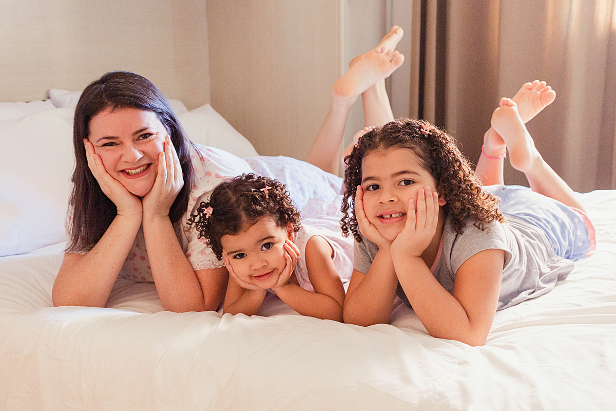 Mãe e filhas fazendo pose na cama para o ensaio de família em casa na zona leste de São Paulo