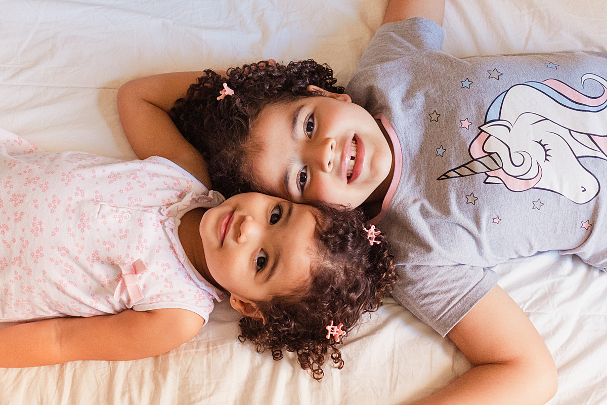 Irmãs se abraçando deitada com rosto colado no ensaio infantil em casa na cidade de São Paulo