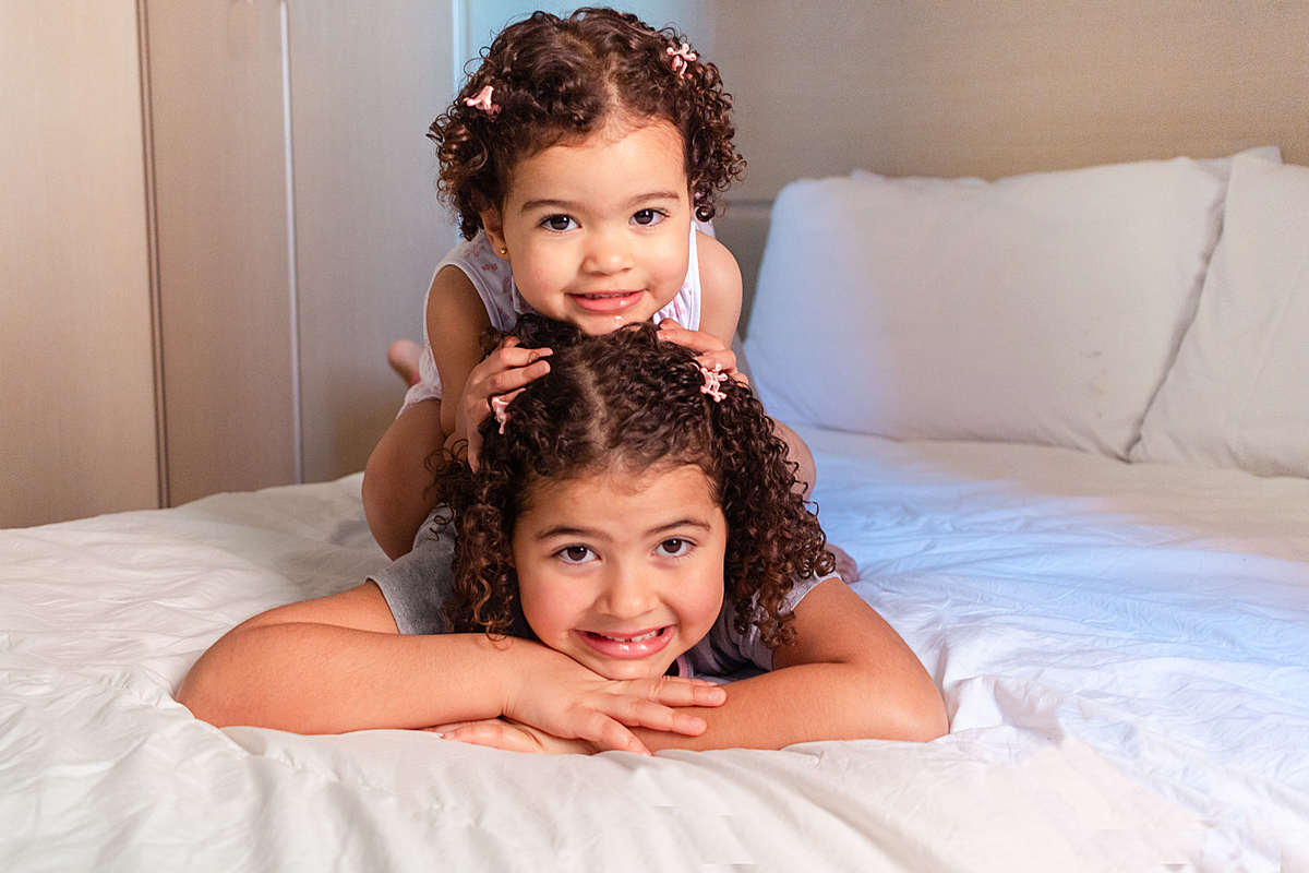 Irmãs se abraçando deitada em cima da outra no ensaio infantil em casa na cidade de São Paulo
