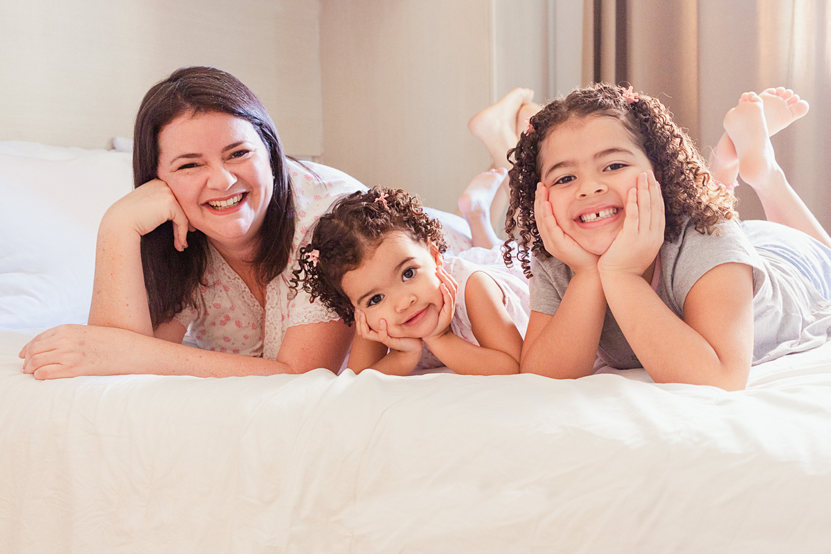 Mãe e filhas fazendo pose na cama para o ensaio de família em casa na zona leste de São Paulo