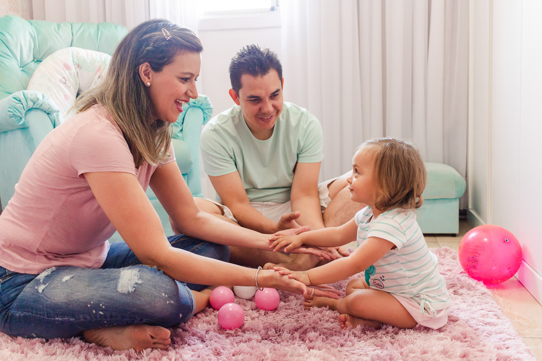 Pais brincando de bolinha com a filha no quarto de menina no ensaio na cidade de São Paulo