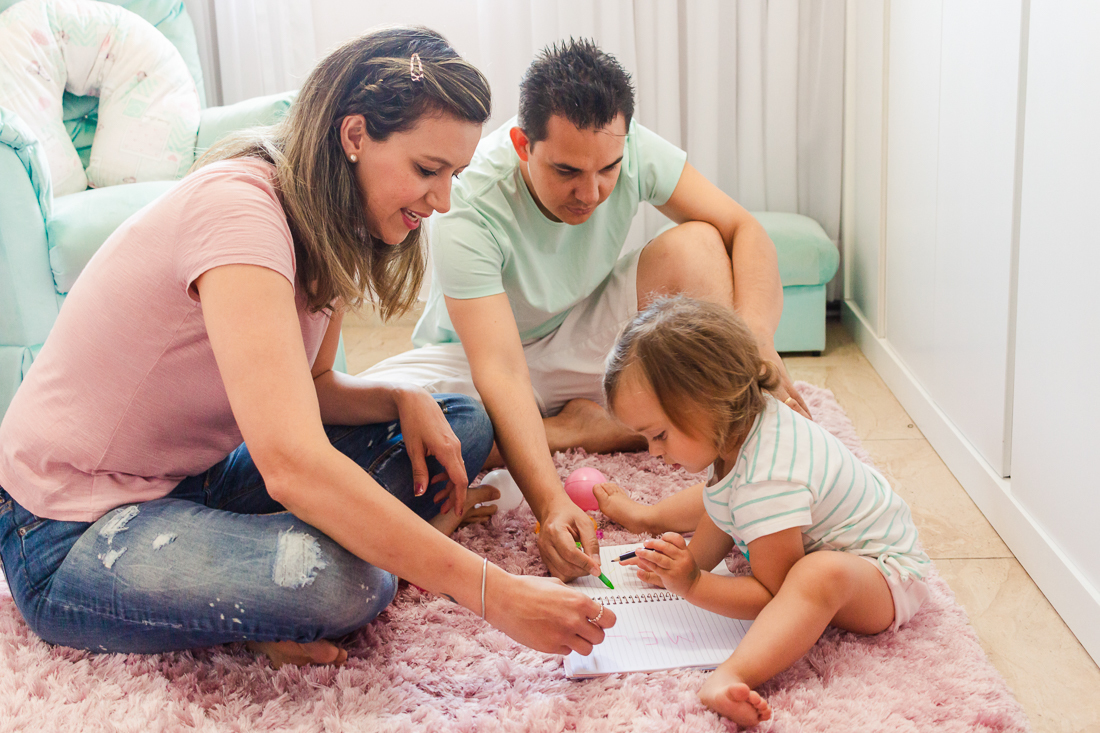 Pais brincando de escrever e desenhar com a filha no quarto de menina no ensaio na cidade de São Paulo
