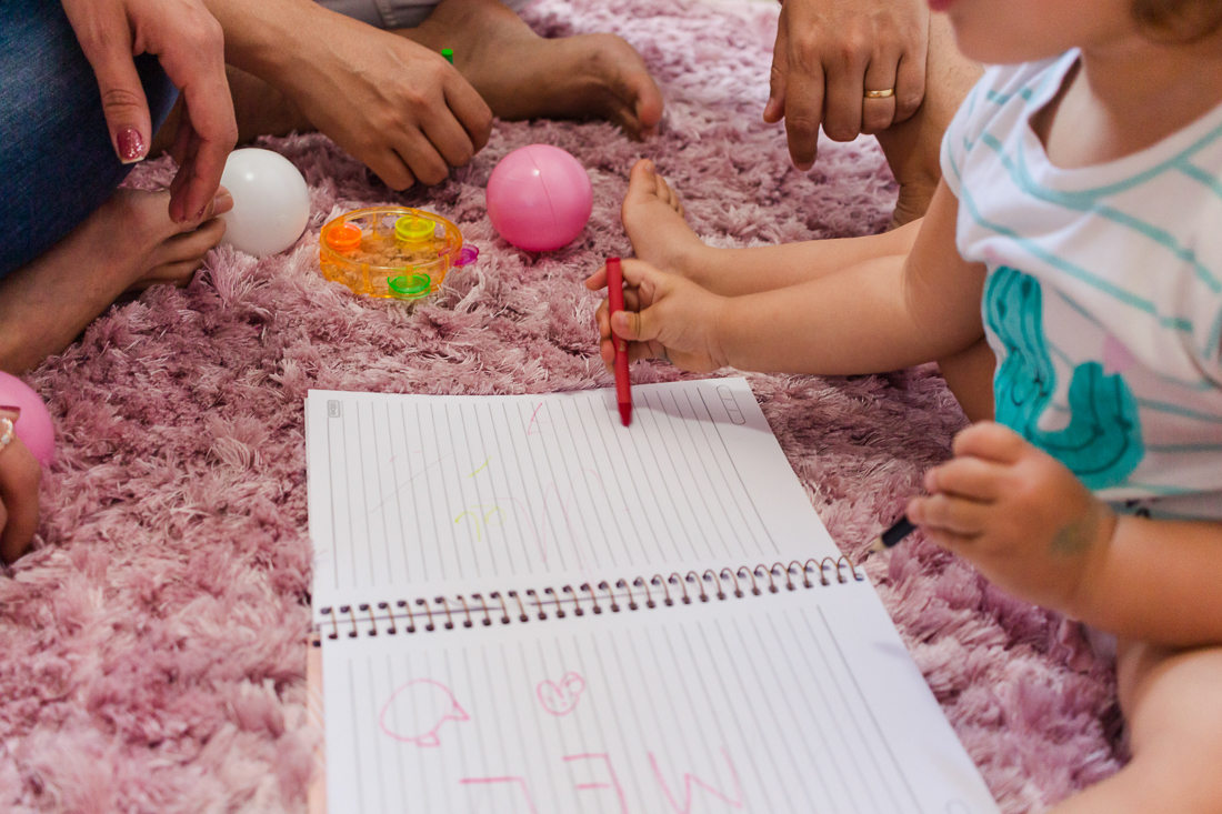 Pais brincando de escrever e desenhar com a filha no quarto de menina sentados no chão no ensaio na cidade de São Paulo