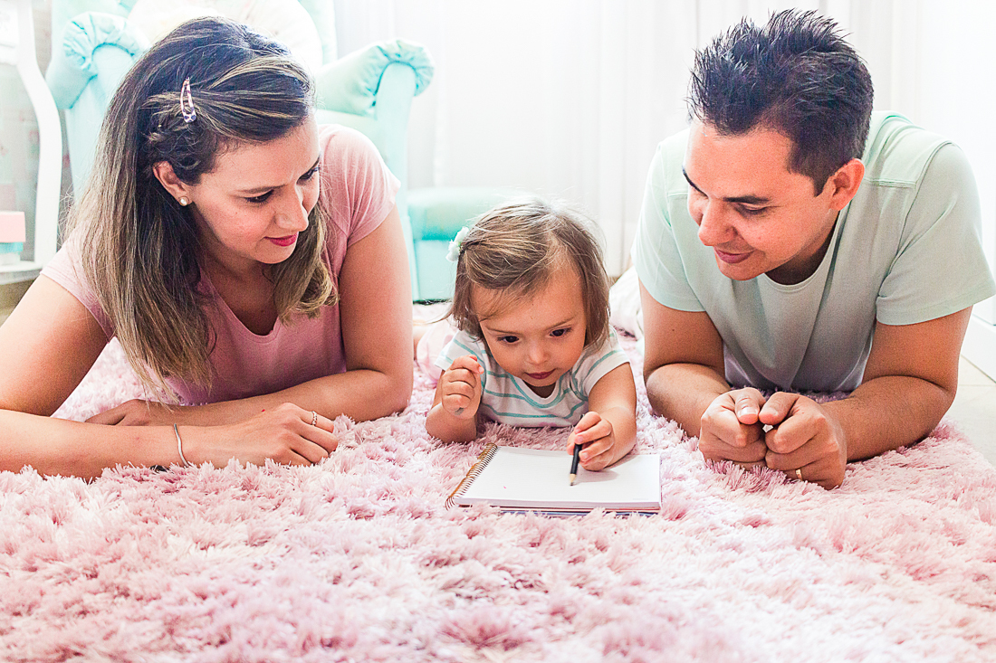 Pais brincando de escrever e desenhar com a filha no quarto de menina deitados no chão no ensaio na cidade de São Paulo