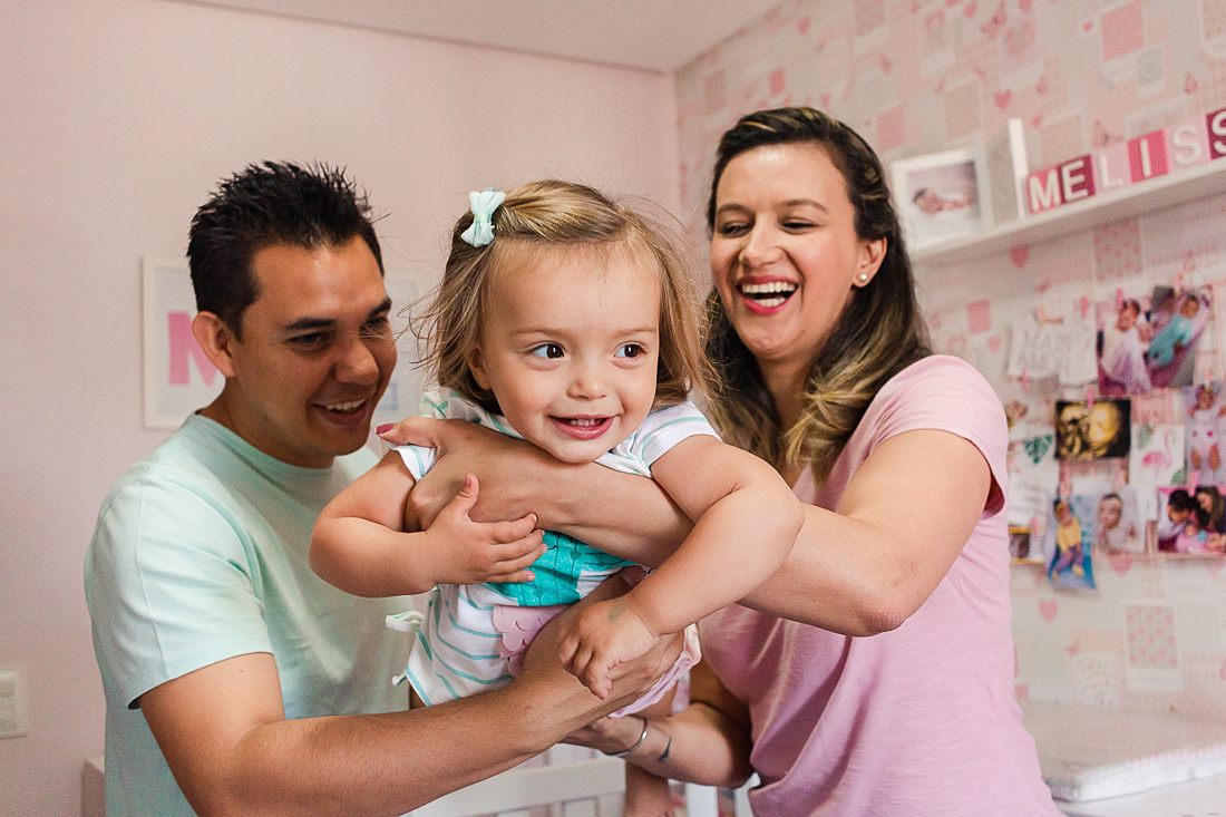 Pais brincando de aviãozinho com a filha no colo sorrindo no ensaio de família na cidade de São Paulo