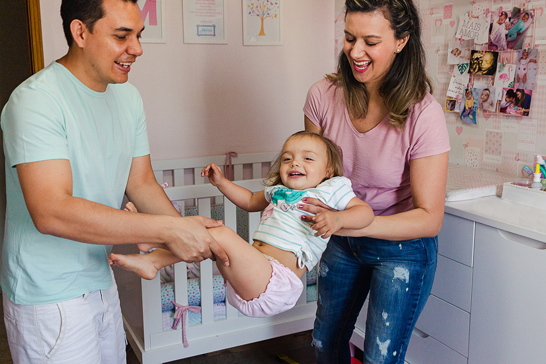 foto de pais brincando de balançar a filha no colo  com a filha no quarto na cidade de São Paulo.