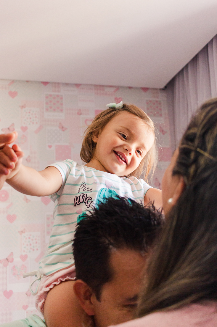 Filha menina no colo do pai e sorrindo para a mãe no ensaio lifestyle na cidade de São Paulo 
