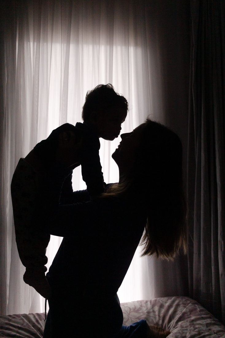 Foto de mãe e filho PB de silhueta se olhando e sorrido no ensaio lifestyle de família em casa 