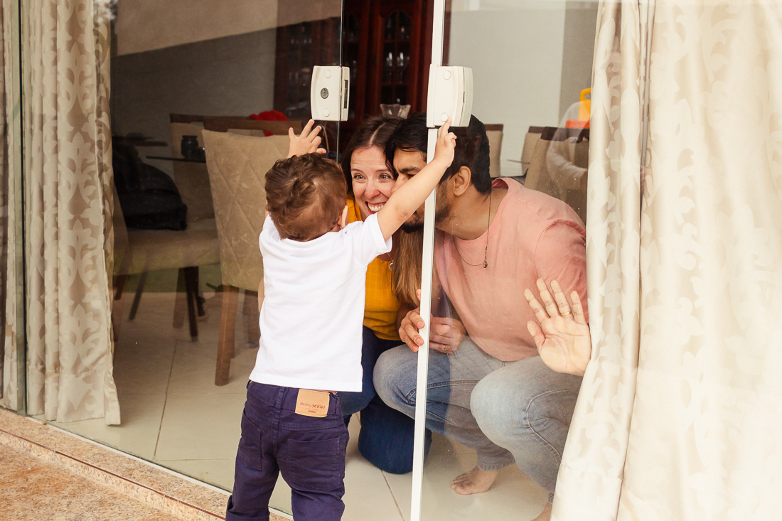 foto de pai e mãe brincando com o filho em casa na porta da sala no ensaio de família na cidade de São Paulo