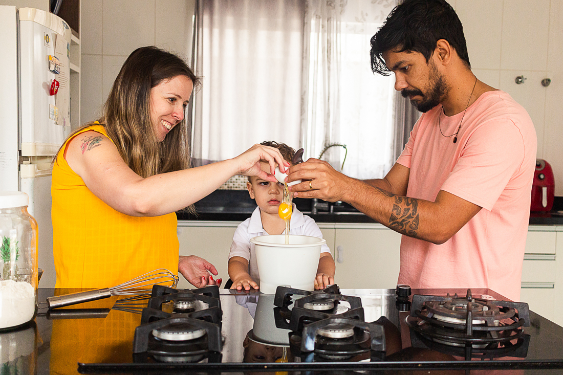 Foto de pais e filho quebrando ovos para fazer uma receita juntos na cozinha de casa no ensaio lifestyle de família na cidade de São Paulo.