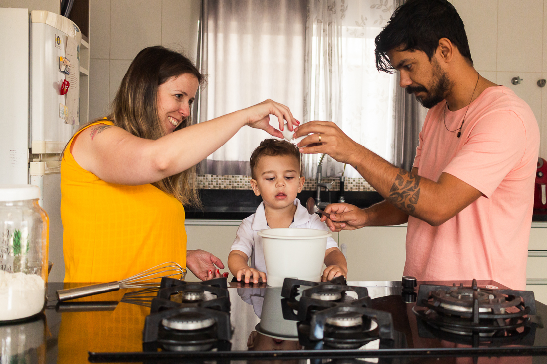 Foto de pais e filho quebrando ovos para fazer uma receita juntos na cozinha de casa no ensaio lifestyle de família na cidade de São Paulo.