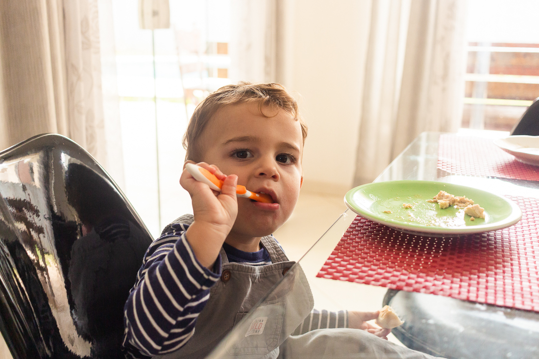 foto de menino  comendo sozinho na mesa da cozinha no ensaio infantil em casa