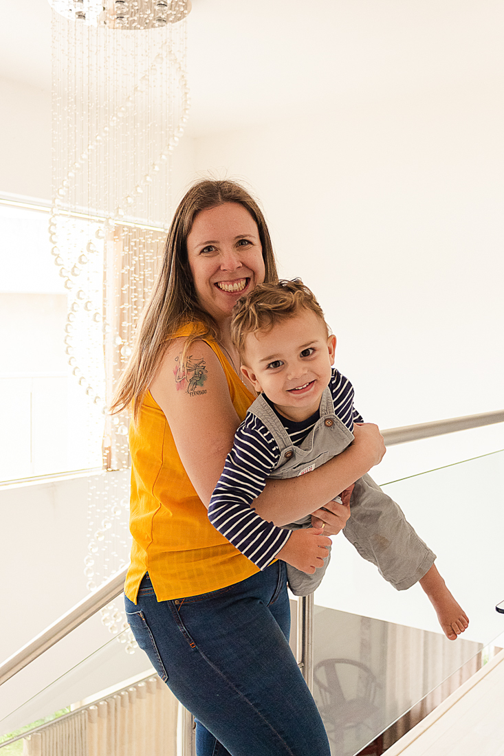 Mãe segurando filho e sorrindo em casa no ensaio de família na cidade de São Paulo.