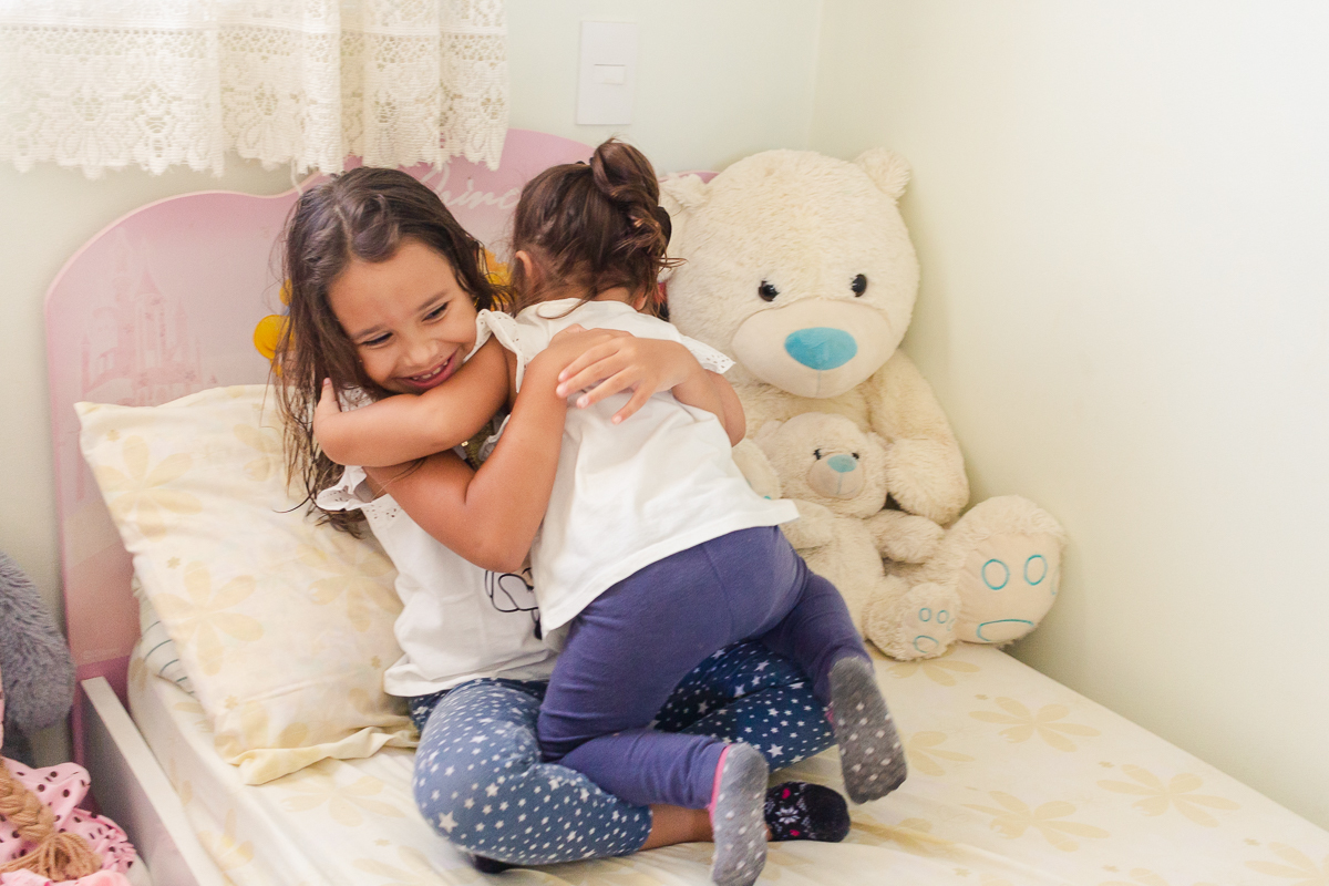 Foto de irmãs se abraçando na cama do quarto das princesas no ensaio infantil em casa na cidade de Franco da Rocha- São Paulo