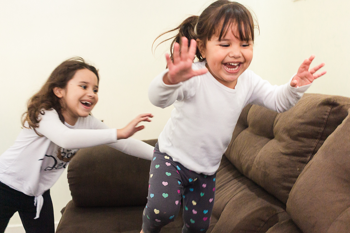 Foto de irmãs brincando de pega pega no sofá de casa no ensaio lifestyle infantil na cidade de Franco da Rocha em São Paulo
