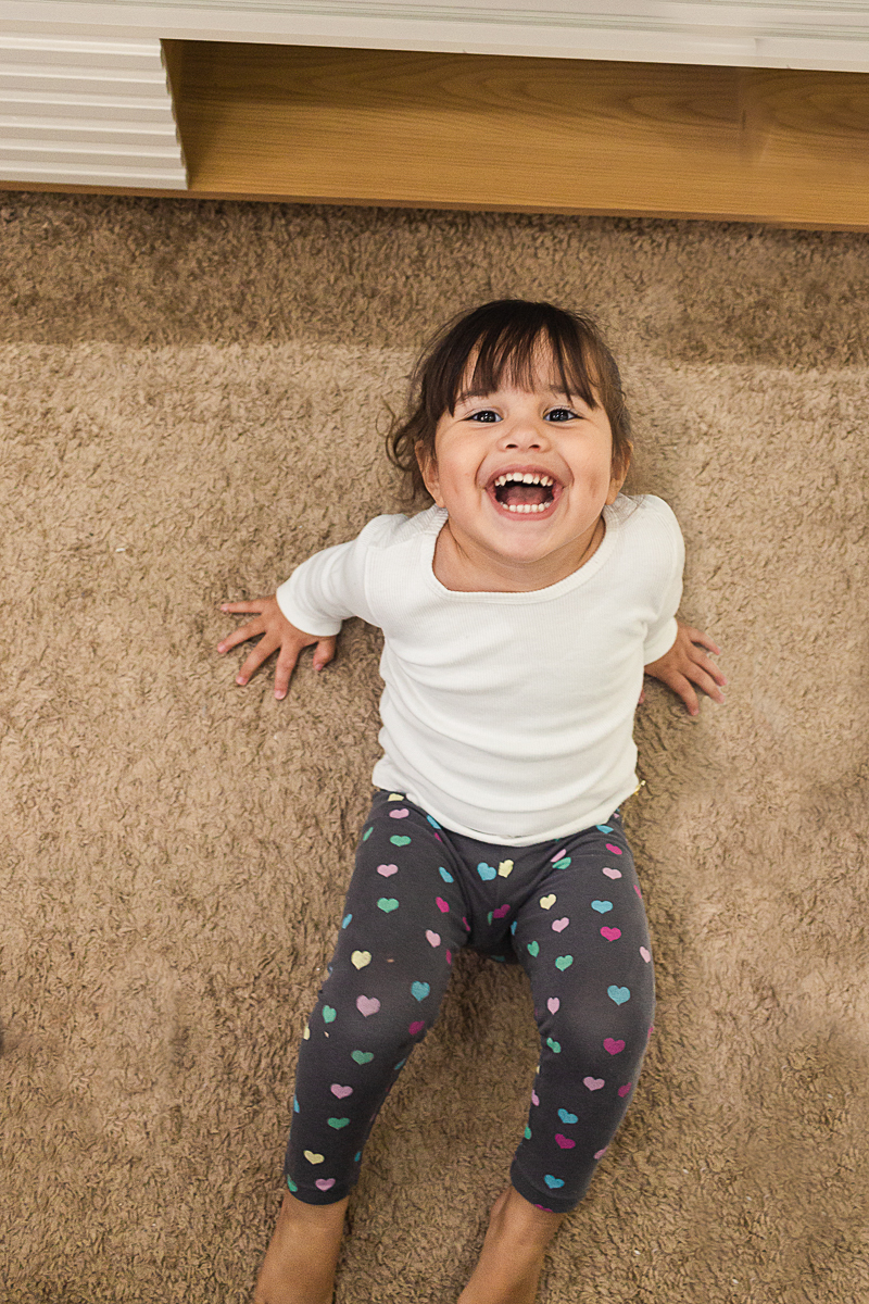 Foto de menina sorrindo no chão da sala de casa no ensaio lifestyle infantil na cidade de Franco da Rocha em São Paulo